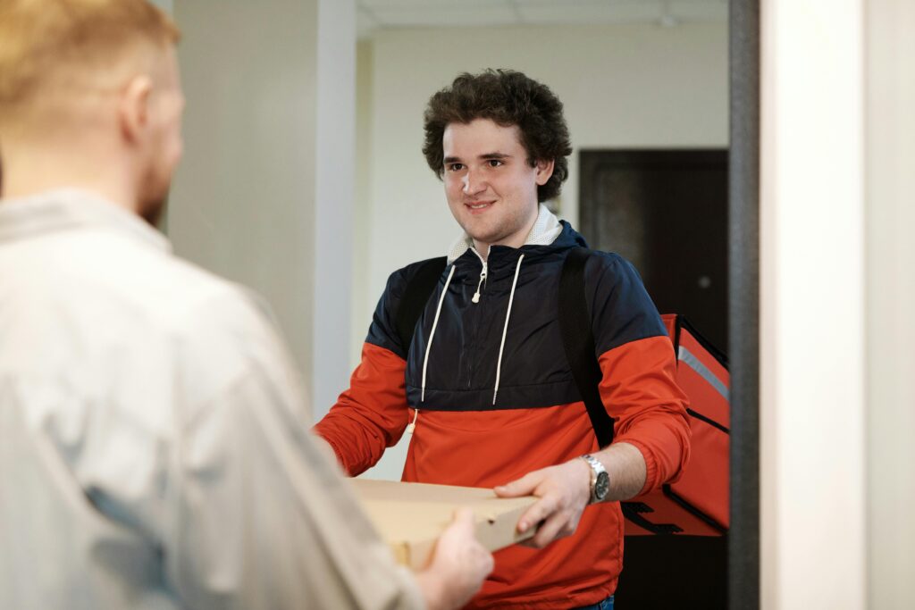 Pizza delivery man in casual wear delivers pizza box to a customer indoors, smiling
